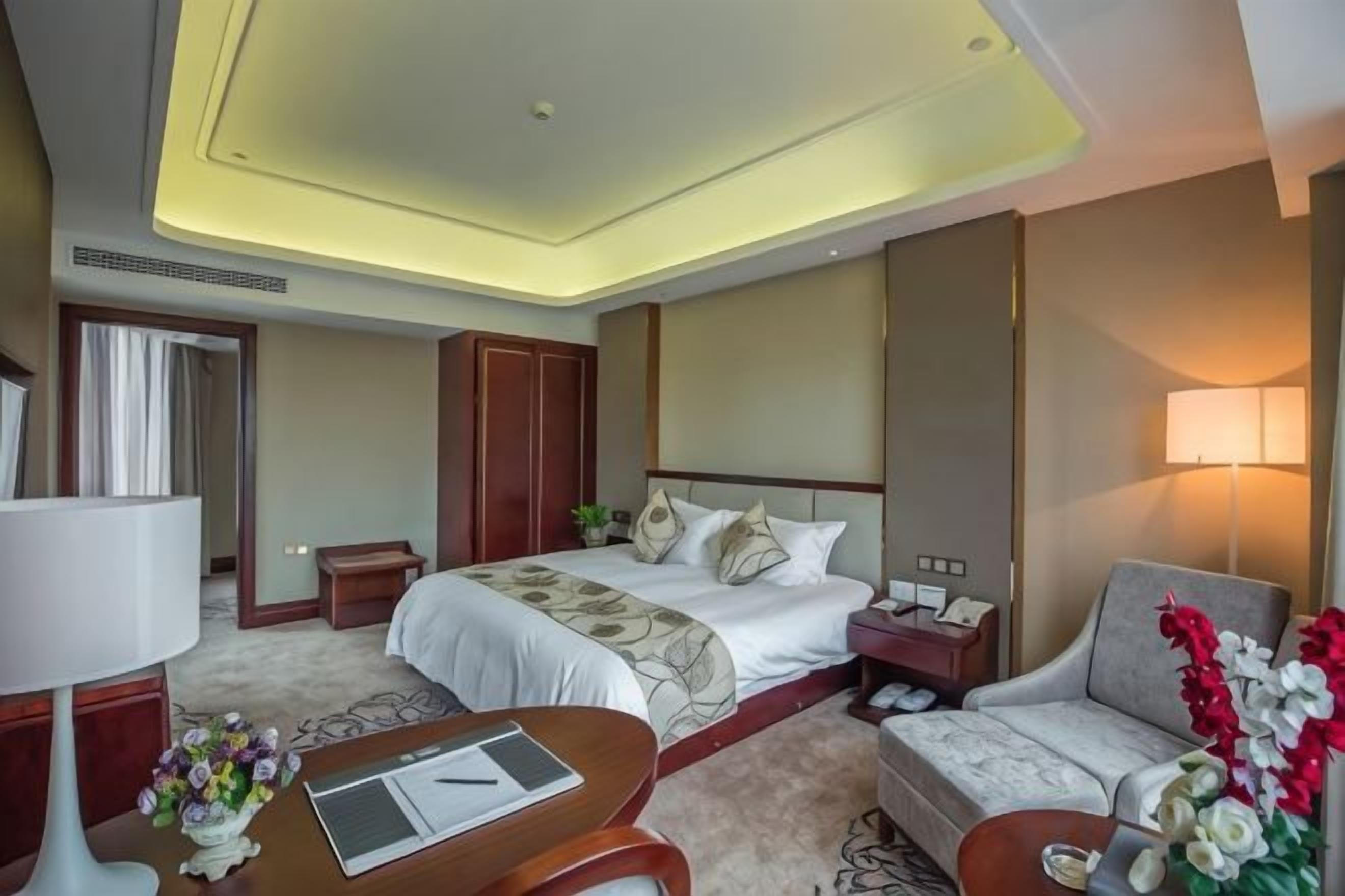 A hotel room with a bed, bedside table, lamp, and a sofa.