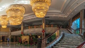 Un lobby espacioso con pisos de mármol, una escalera central y grandes candelabros.