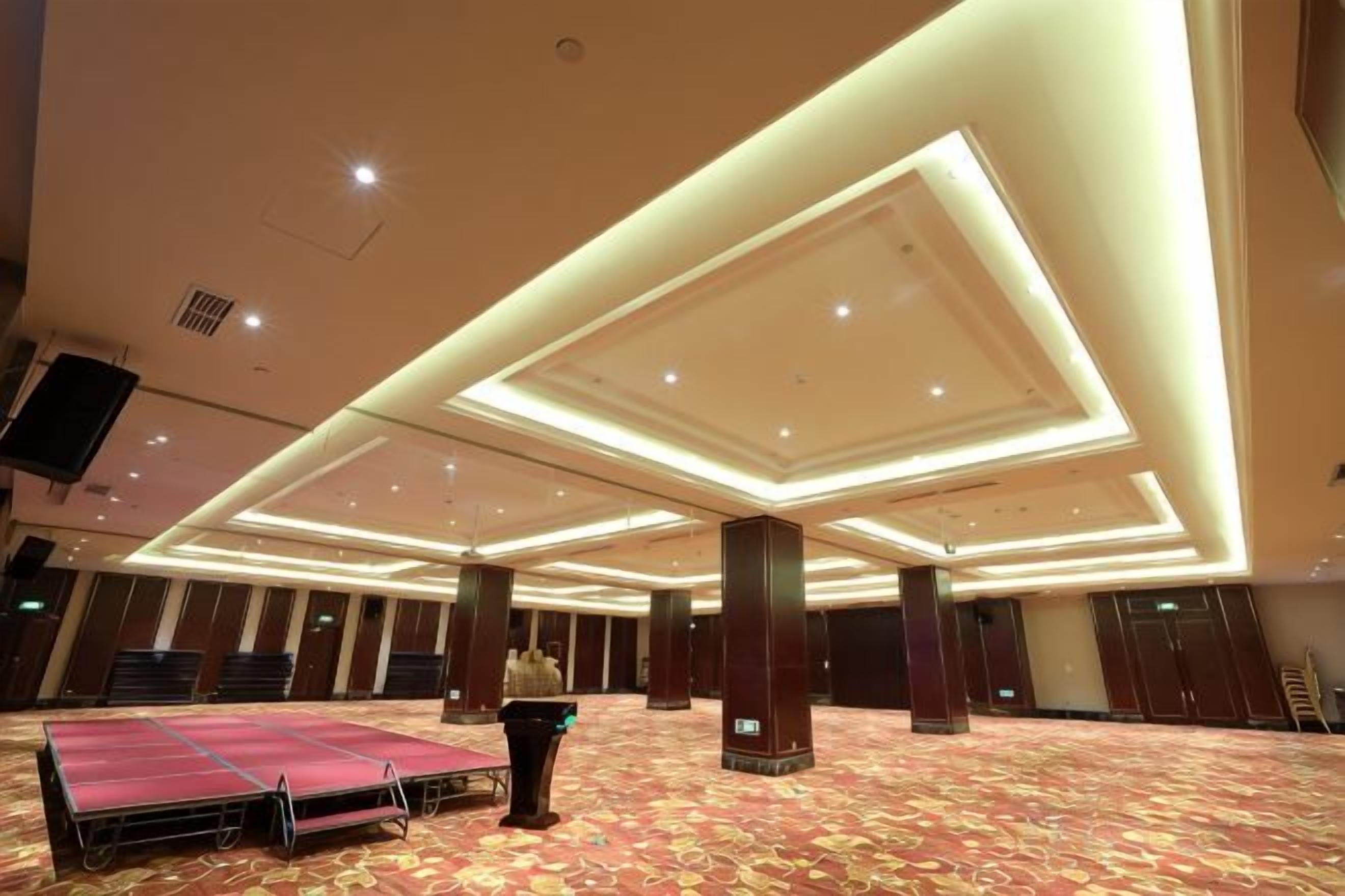 Un salón amplio con un escenario, hileras de sillas y suelo alfombrado.