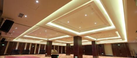 Un salón amplio con un escenario, hileras de sillas y suelo alfombrado.