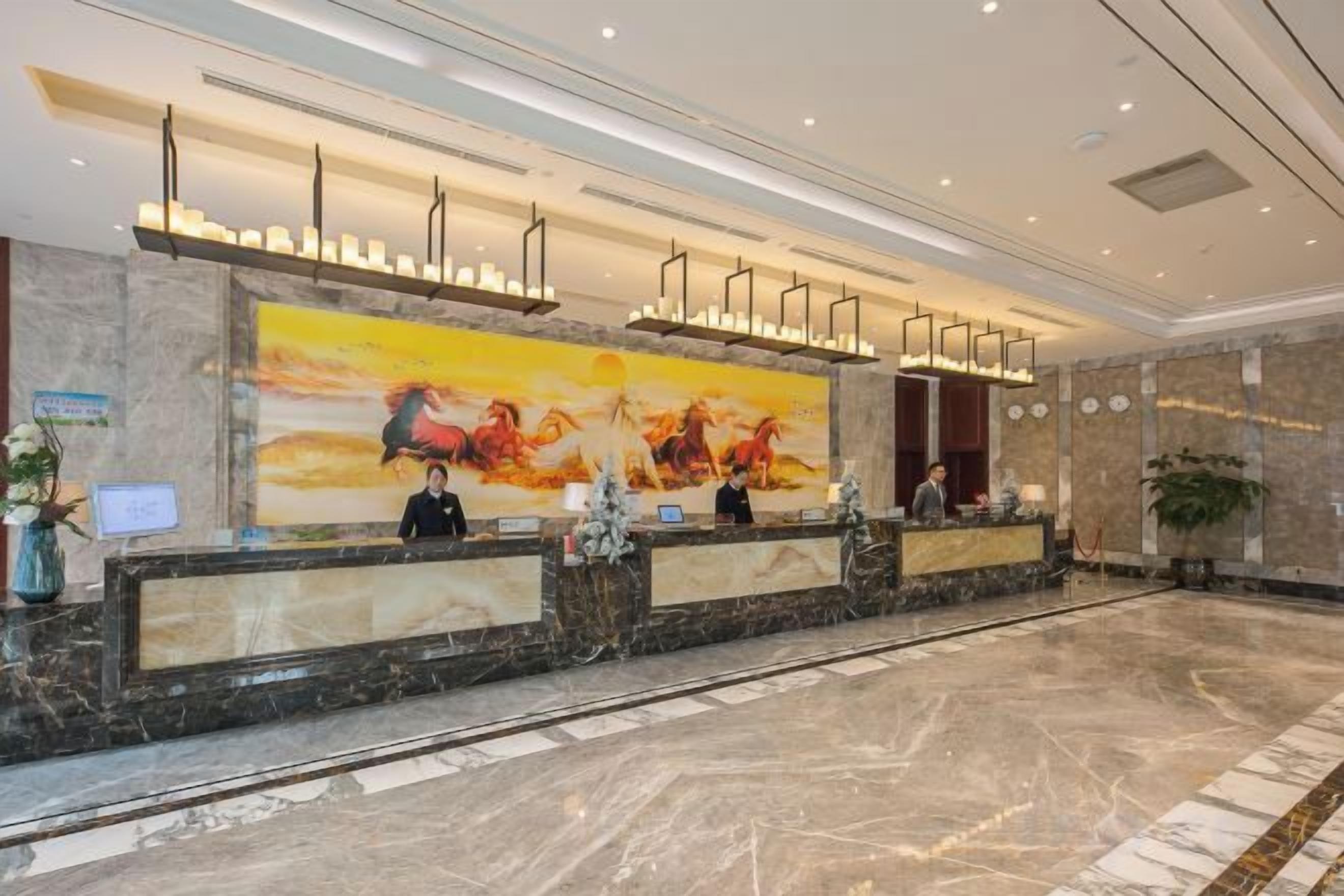 A hotel reception area with a marble floor, a large painting of horses, and a reception desk with two staff members.