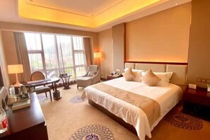 Habitación de hotel con una cama grande, un escritorio con lámpara, una silla y vistas al exterior por la ventana.