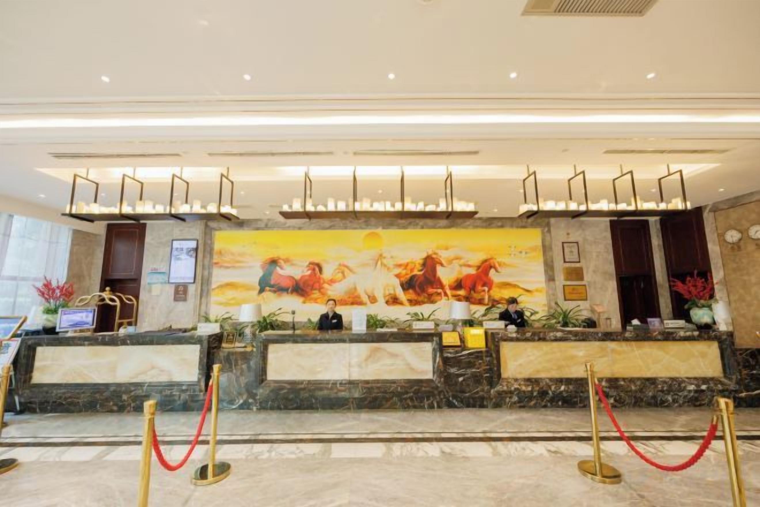 A hotel reception area with marble counters, a large mural, and a modern chandelier.