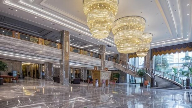 Un vestíbulo amplio con suelo de mármol, grandes candelabros, una escalera y vistas al exterior.