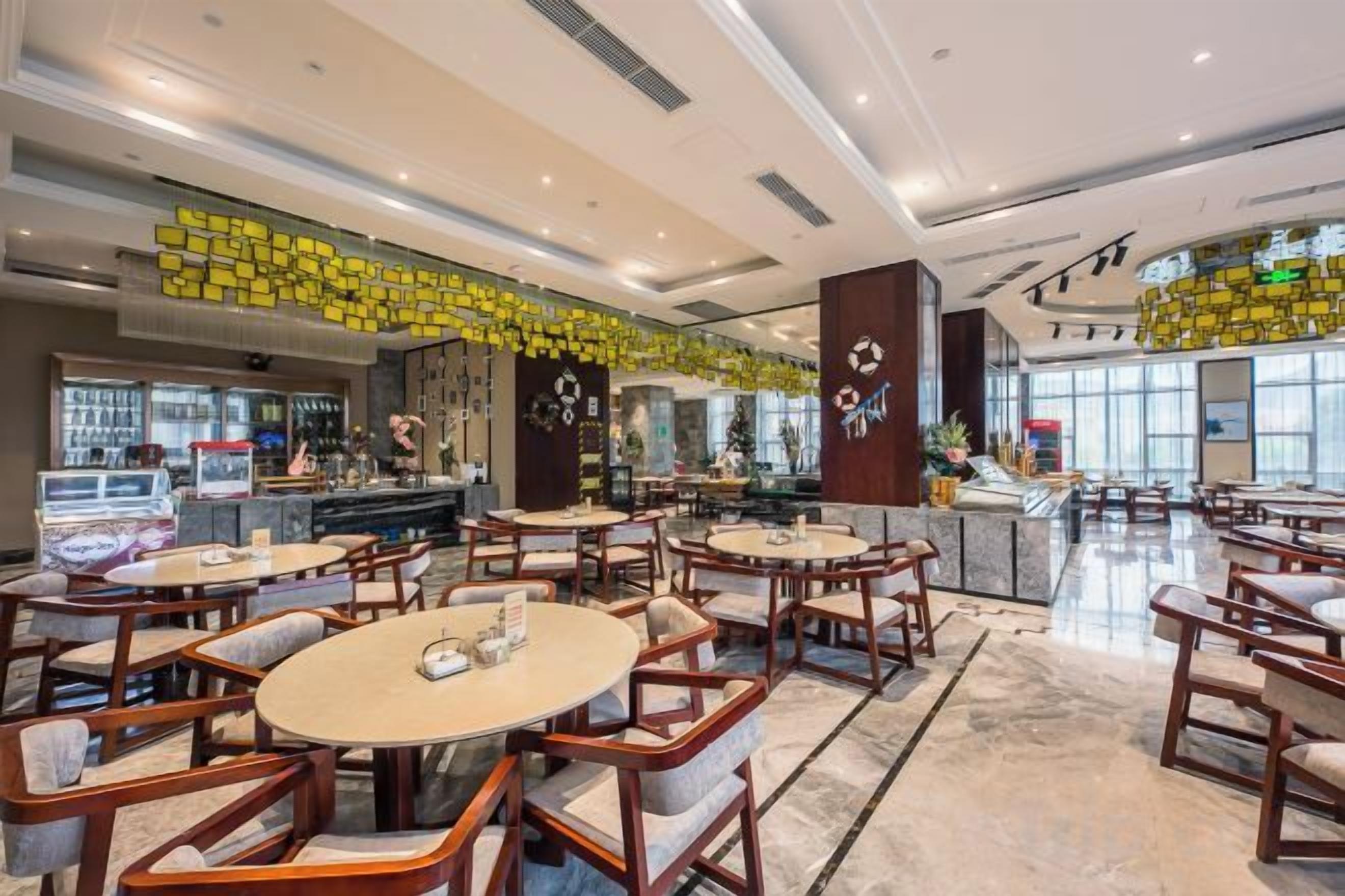 A spacious indoor area with multiple round tables and chairs, a bar area, and a large window providing natural light.