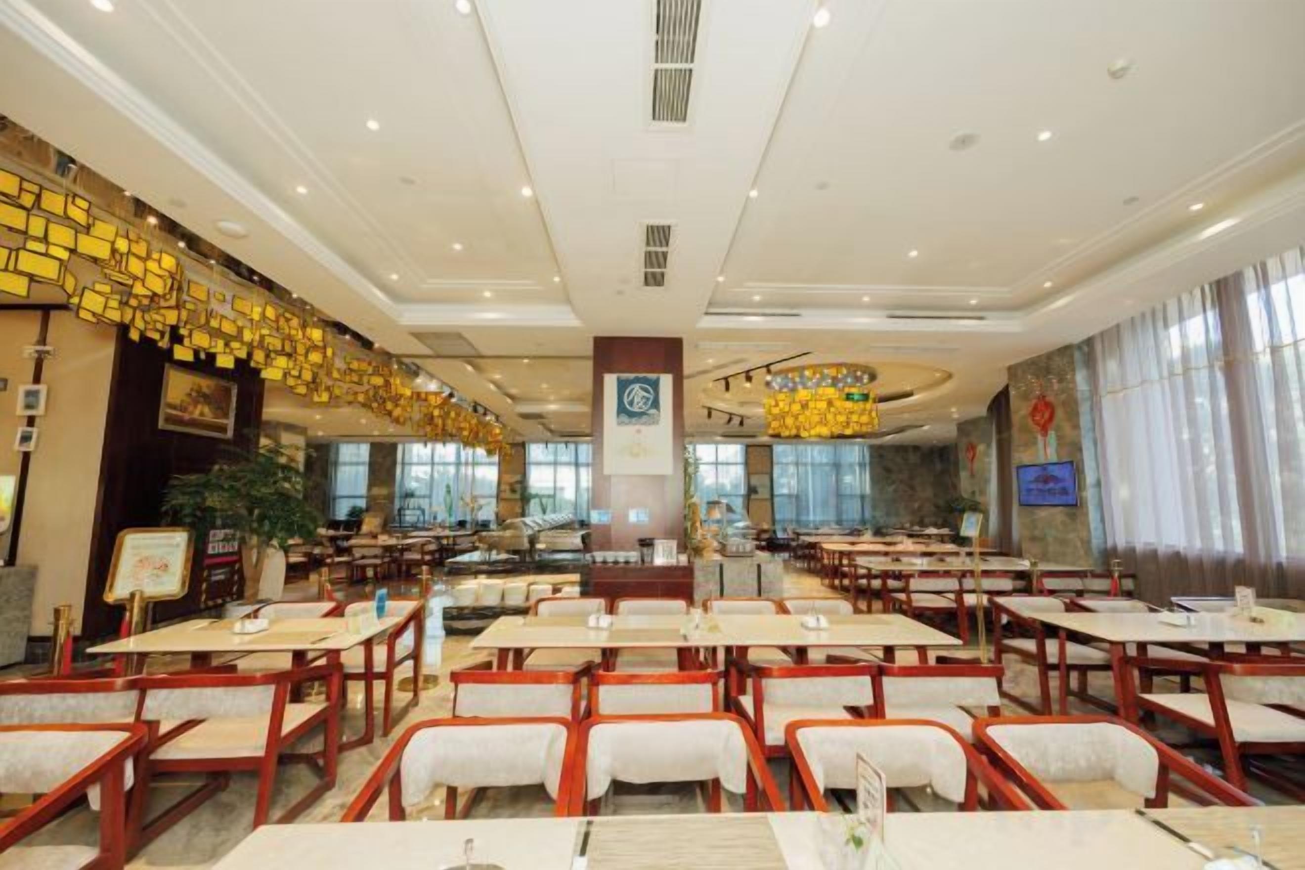 A spacious restaurant with multiple tables and chairs, a central pillar, and a large window providing natural light.