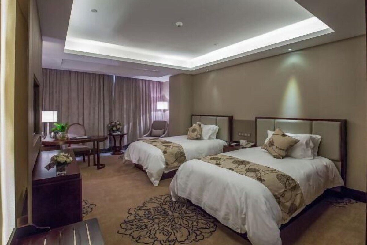 A hotel room with two beds, a desk, a chair, and a large window with curtains.