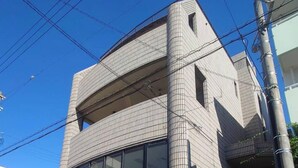 A multi-story building with a tiled facade, a gated entrance, and a small shop with a tiled roof. - Guest house Blue Ocean Naha - Hostel  (Naha)