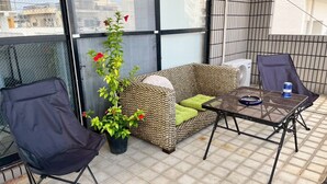 A balcony with a wicker sofa, two chairs, a small table, and a potted plant. - Guest house Blue Ocean Naha - Hostel  (Naha)
