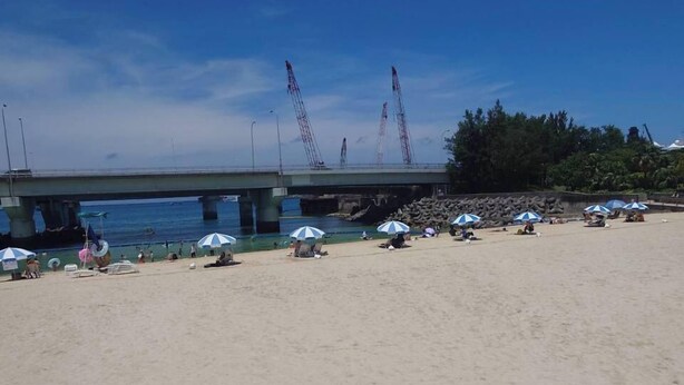 A beach with a bridge in the background, umbrellas, and people relaxing. - Guest house Blue Ocean Naha - Hostel  (Naha)