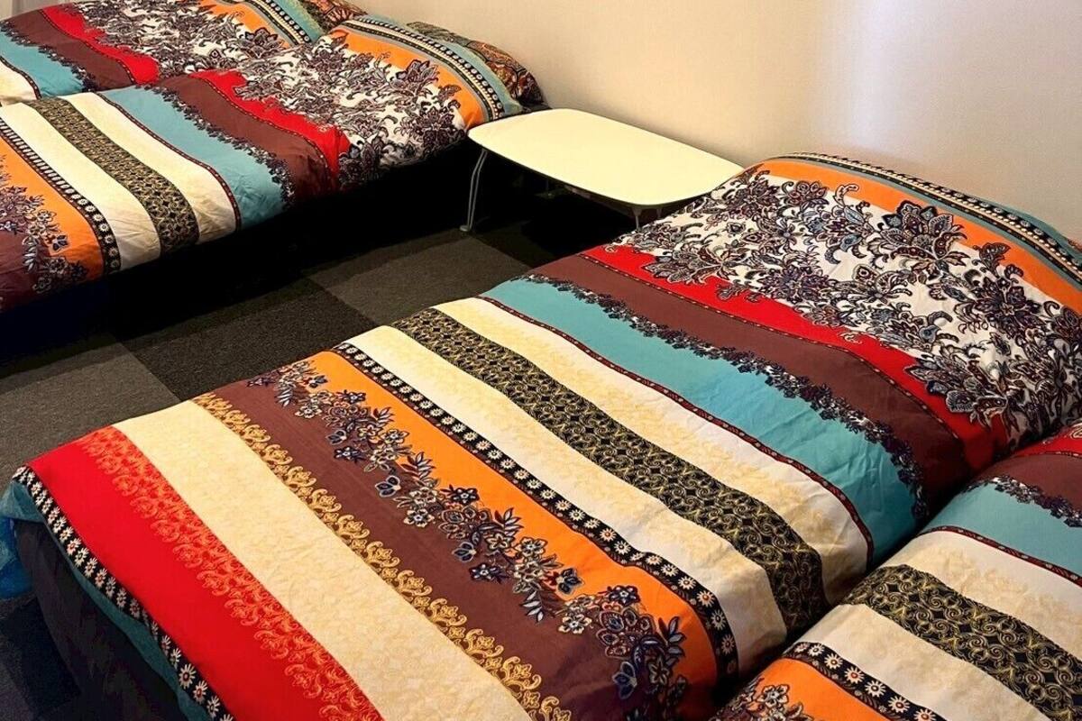Una habitación con dos camas, cada una con una colcha estampada, una mesita pequeña y adornos en la pared, incluyendo un cuadro enmarcado y diseños circulares.