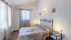 A hotel room with a bed, two bedside tables, a window with curtains, an air conditioning unit, and wall-mounted lights. - Casa Rueapara Torrox by Ruralidays (Málaga)