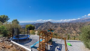 A playground with a trampoline and a wooden play structure, set against a backdrop of mountains and clear skies. - Casa Rueapara Torrox by Ruralidays (Málaga)