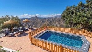 A swimming pool with a wooden fence, lounge chairs, and a view of mountains. - Casa Rueapara Torrox by Ruralidays (Málaga)