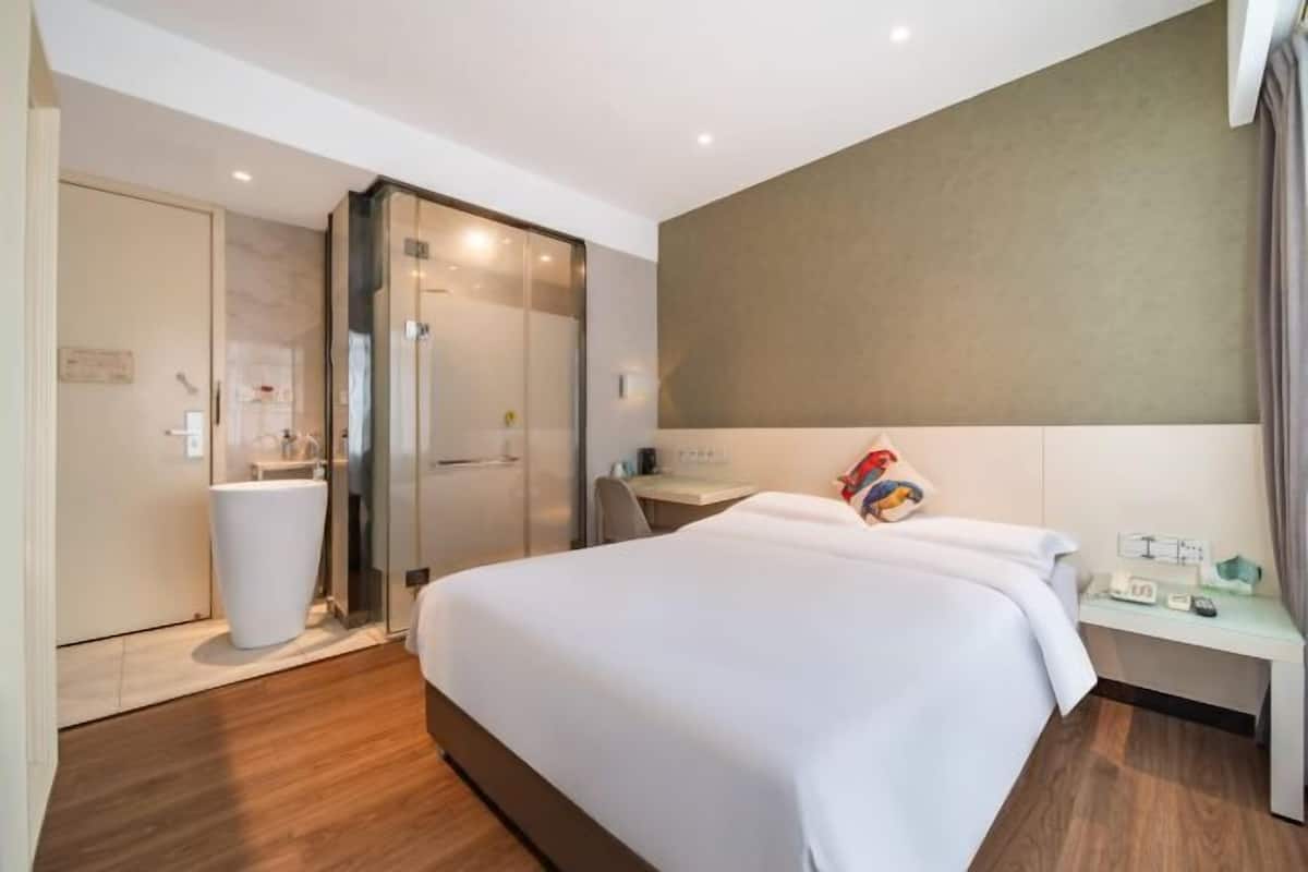 Una habitación de hotel con cama, mesita de noche y zona de ducha.