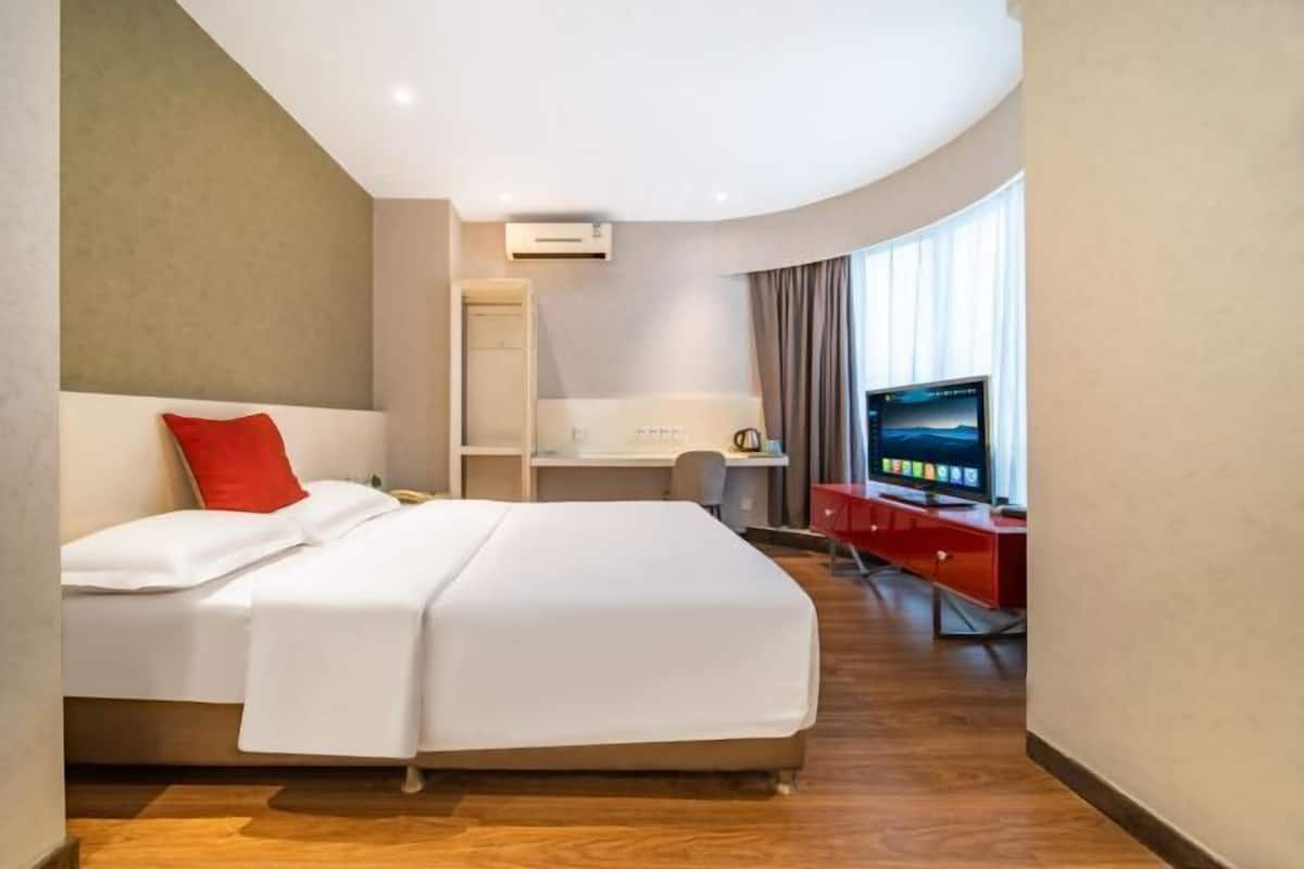 Una habitación de hotel con cama, escritorio, televisor y armario.