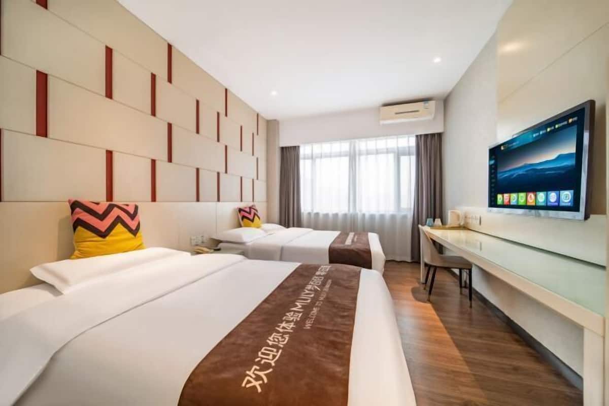 Habitación de hotel con dos camas, un televisor de pantalla plana, un escritorio y una ventana con cortinas.