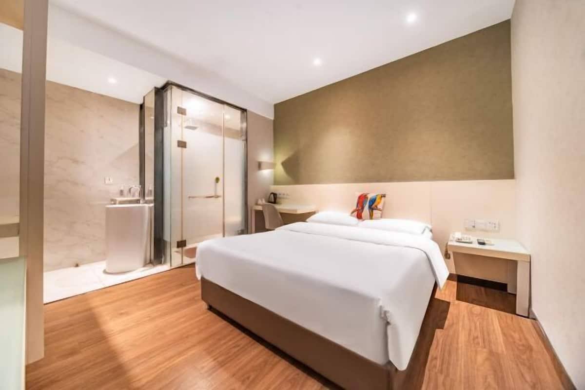 Una habitación de hotel moderna con una cama grande, una mesita de noche, un escritorio y una zona de ducha.