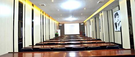 A conference room with long tables and chairs, a projector screen, and a presentation screen.