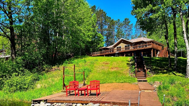 Eine Holzterrasse mit Stühlen an einem ruhigen Teich, eine Holztreppe, die zu einer Lodge führt, und üppiges Grün im Hintergrund.