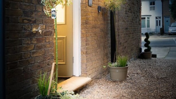 A brick building with a white door, potted plants, and a gravel pathway. - Stylish Modern Designed Apt, near Station, London (Northwood)
