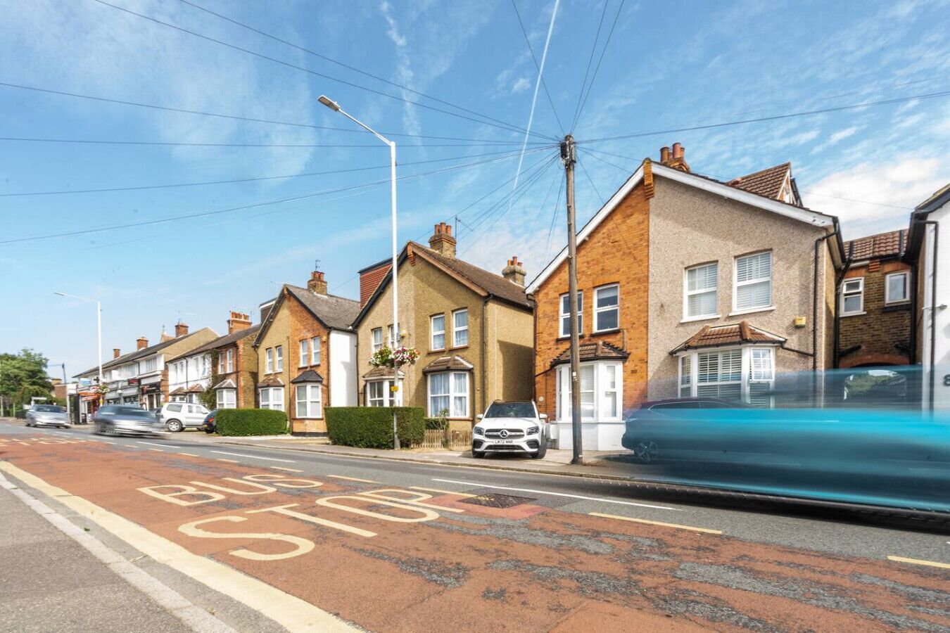 A residential street with terraced houses, a clear blue sky, and a bus stop sign on the road.