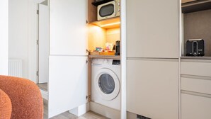 A compact kitchen with a washing machine, microwave, and a small countertop with kitchenware. - Stylish Modern Designed Apt, near Station, London (Northwood)