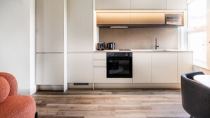 A modern kitchen with white cabinetry, a black oven, and a window providing natural light. - Stylish Modern Designed Apt, near Station, London (Northwood)