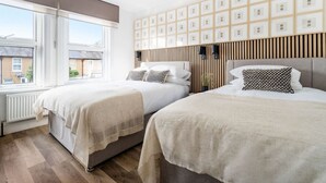 A hotel room with two beds, a large window, a wall with framed pictures, and a modern light fixture. - Stylish Modern Designed Apt, near Station, London (Northwood)