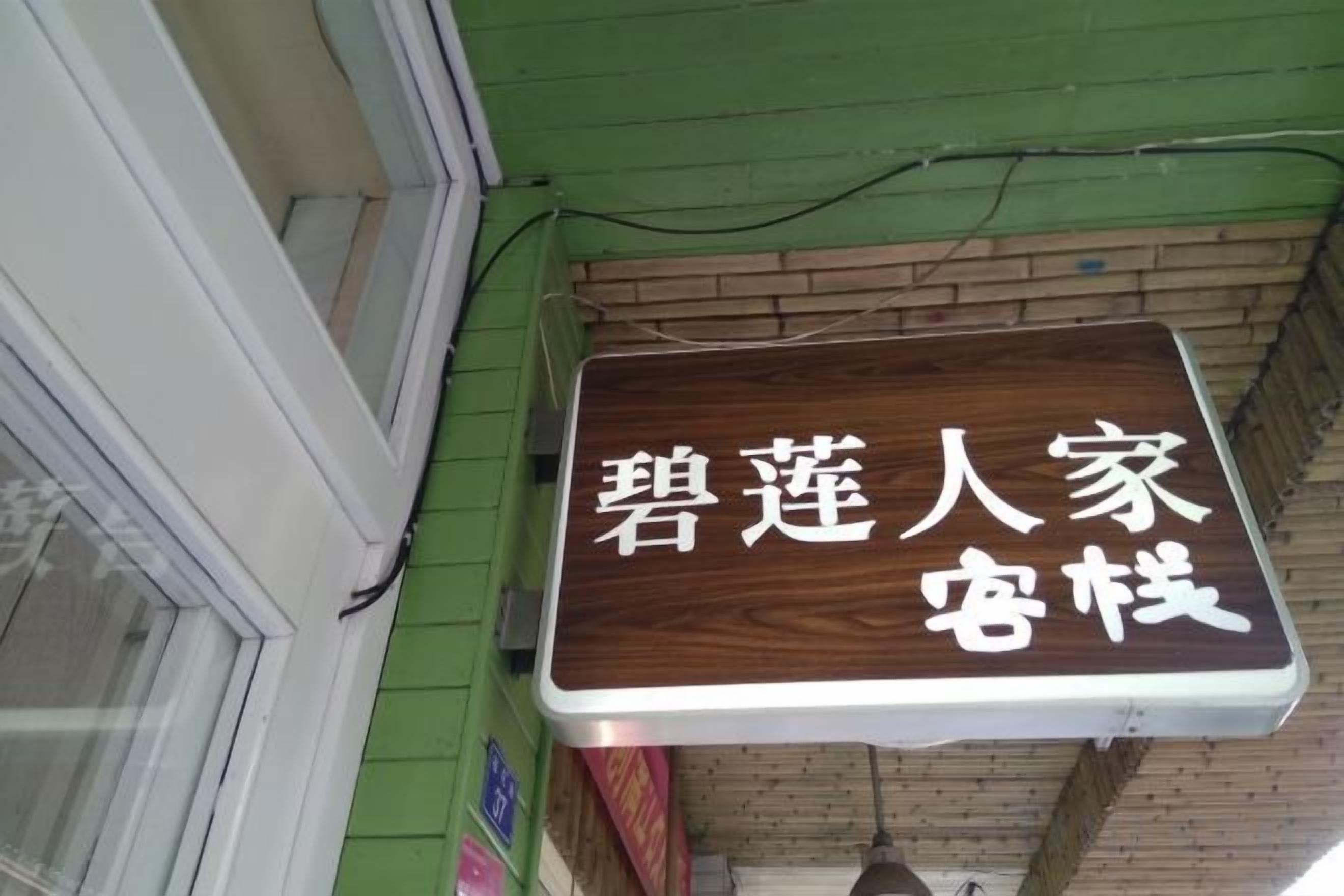 A sign with Chinese characters on a wooden board, mounted on a brick wall.