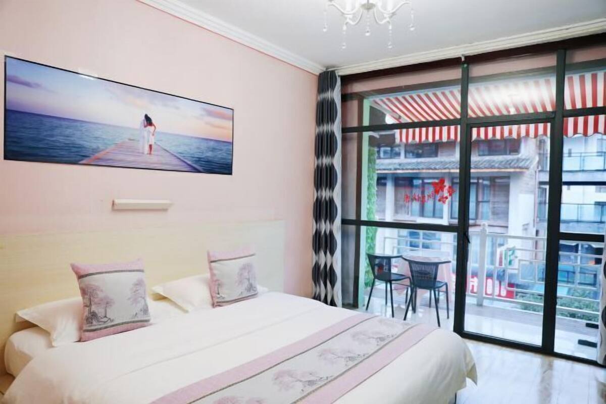 A bedroom with a large bed, a view of the sea through a window, and a balcony with a striped awning.