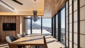 A modern dining area with a large table, chairs, and a view of a snowy landscape through large windows. - Dharma Niseko (Kutchan)