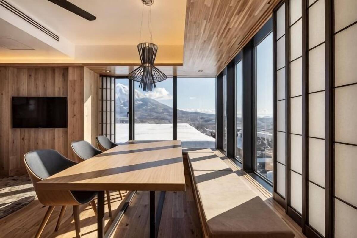 A modern dining area with a large table, chairs, and a view of a snowy landscape through large windows.