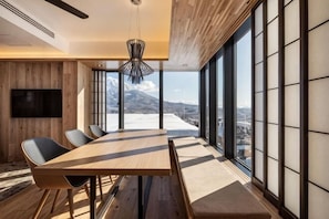 A modern dining area with a large table, chairs, and a view of a snowy landscape through large windows. - Dharma Niseko (Kutchan)
