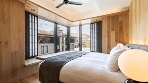 A bedroom with a large bed, wooden walls, a ceiling fan, and a view through large windows. - Dharma Niseko (Kutchan)