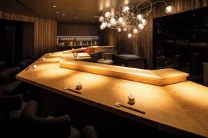 Eine Bar mit einer langen Holztheke, Barhocker und einer hängenden Leuchte.