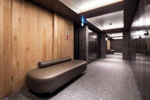 Egy modern lift előtér, amelyben van egy pad, egy a falra szerelt tűzriasztó és egy sor szekrény.