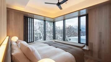 A modern bedroom with a large bed, a ceiling fan, and large windows offering a view of snow-covered trees.