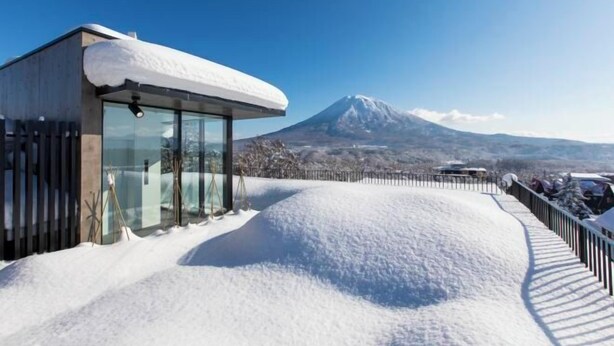 A modern building with large glass windows and a snow-covered roof, overlooking a snow-covered landscape and a mountain. - Dharma Niseko (Kutchan)