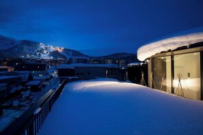 A snow-covered balcony with a view of a mountain and a lit building. - Dharma Niseko (Kutchan)