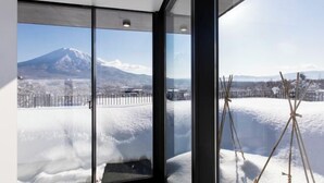 A room with large windows offering a view of a snow-covered landscape and a mountain. - Dharma Niseko (Kutchan)