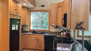 A kitchen with wooden cabinets, a black refrigerator, a stove, and a window with blinds.