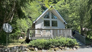 A small cabin with a wooden deck and a stone wall in front.