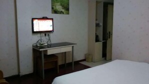 Ein Zimmer mit einem Bett, einem Schreibtisch mit Computer, einem Stuhl und einer Tür zu einem weiteren Raum.