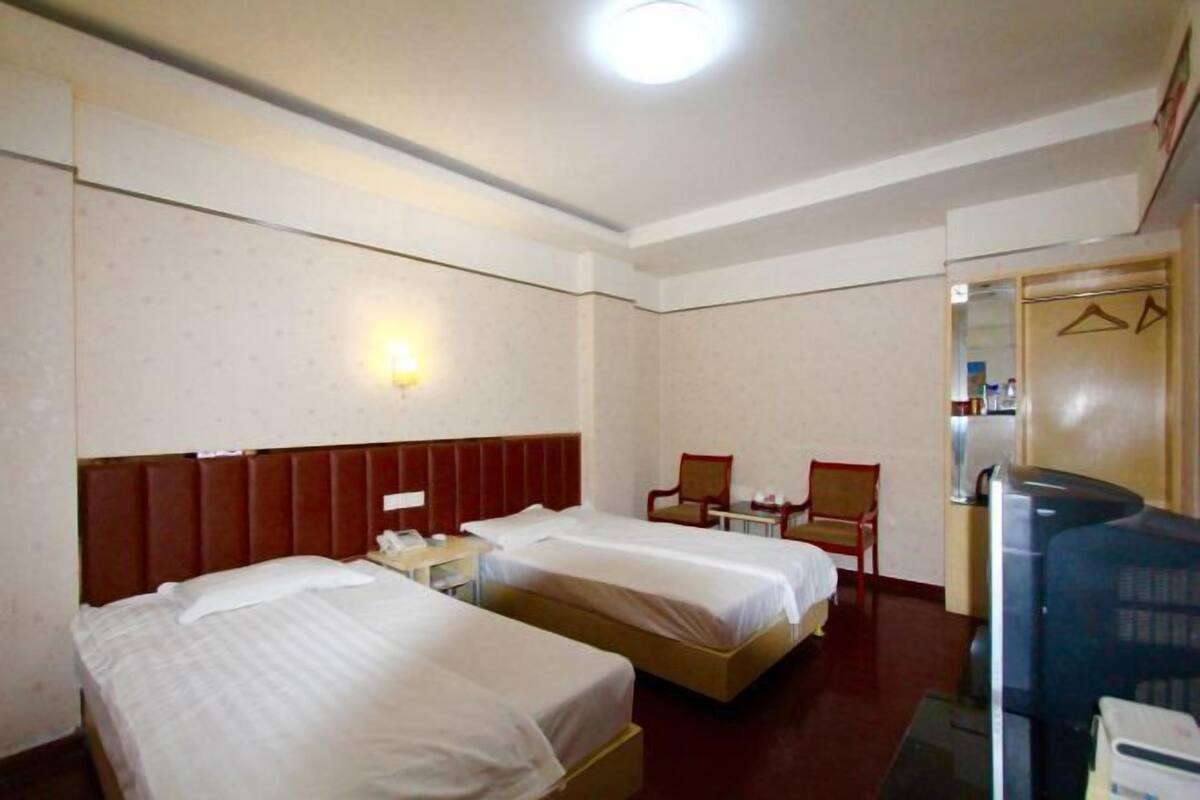 Una camera d'albergo con due letti, una scrivania, una sedia, un televisore e uno specchio.