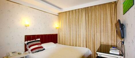 A hotel room with a bed, bedside table, lamp, and curtains.
