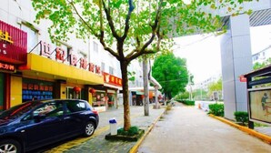 Eine Straße mit einem blauen Auto am Straßenrand, einem Baum in der Mitte und Gebäuden mit Schaufenstern.