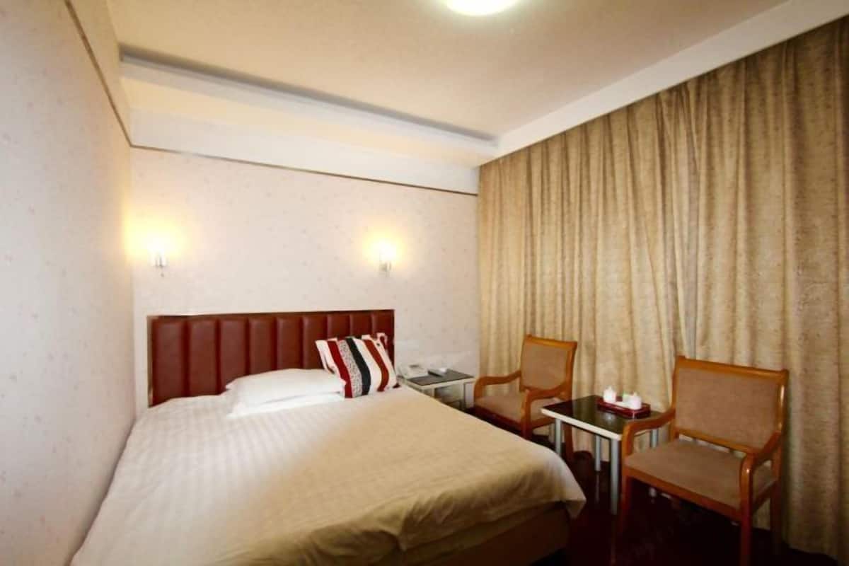 Una camera d'albergo con un letto grande, due abat-jour, un tavolino con una sedia e una tenda che copre la finestra.