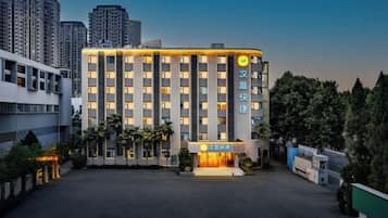 A multi-story hotel with a modern facade, a central entrance, and a parking area in front.