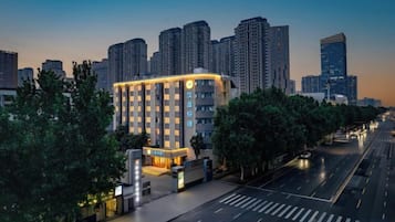 A modern hotel with a prominent entrance, surrounded by trees and set against a city skyline.